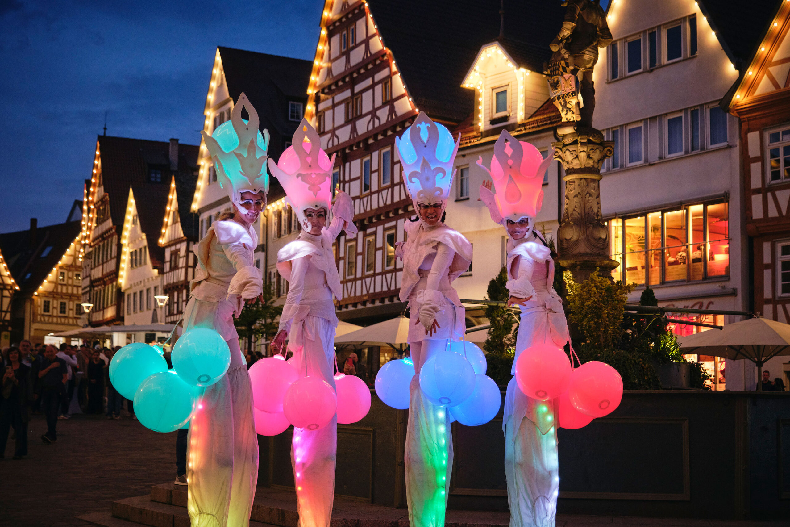 Vier bunte Lichtwesen von Hochkant vor Fachwerkhäusern
